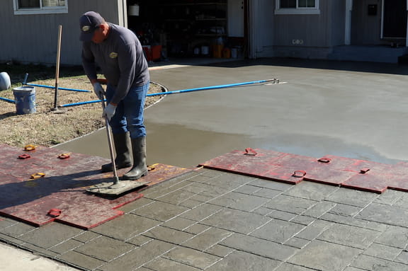 Contractor stamping a residential concrete driveway to create a stone pattern.